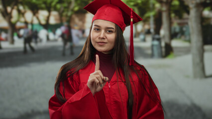 Young woman in graduation cap and gown poses outdoors on a street, celebrating education...