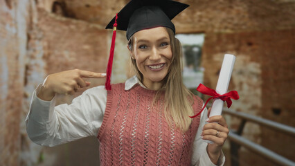 Young blonde woman wearing graduation cap and holding a diploma smiles in front of roman ruins,...