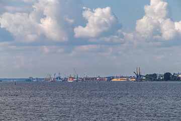 View from the water to the port area with cranes and ships. Cargo ships with containers, sea freight transportation