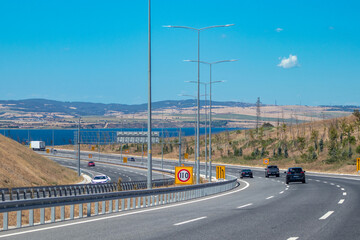 Under clear blue skies, the 1915 Çanakkale Bridge, with its impressive red towers and modern suspension bridge design, spans the Dardanelles in Turkey