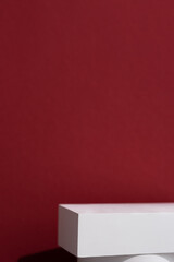 Geometric white scene on a burgundy background. A premium podium for advertising and presentation of your product. Showcase, display case.