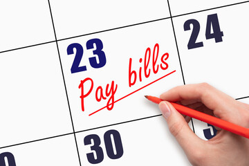 23rd day of the month.  Hand writing Pay bills reminder and drawing a line on calendar with red pen...