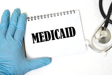 doctor's hand holding a notebook with MEDICAID written on a white background.