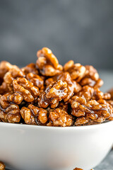 Obraz premium Close-up of glazed walnuts piled high in a white bowl, showcasing their rich, caramelized coating and enticing texture against a blurred background.