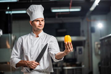 Portrait of Professional Caucasian Male Chef Holding Knife and Bell Pepper in Commercial Kitchen with Confident Expression and Culinary Expertise