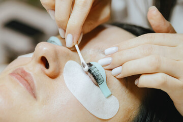 Girl cosmetologist laminates and paints woman eyelashes