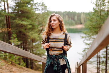 Young woman hiker with a backpack on a walking wooden path overlooking a lake. Woman traveler...