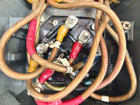 A chaotic yet connected array of thick copper cables and wires, secured with lugs and bolts, highlighting the intricate electrical connections within an industrial control box. The worn and taped wir