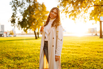 A young woman stands in a sunny park and enjoys a walk. A beautiful woman in stylish clothes relaxes outdoors. Walking, beauty and fashion concept.