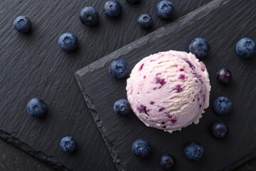 Captivating scoop of blueberry ice cream enhanced with berry bits on black slate surrounded by fresh blueberries top-down view for a delicious treat experience