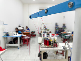 Close-up image of red threads in a garment workshop with blurred seamstresses in the background. Focus on thread path in a sewing machine.