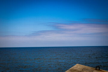 Peaceful ocean scene with gentle waves stretching toward a clear blue horizon, lightly clouded sky,...