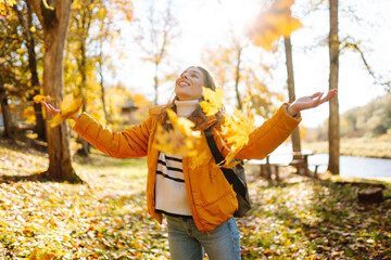 A happy woman stands in an autumn park and cheerfully throws colorful leaves up. A young woman in a...