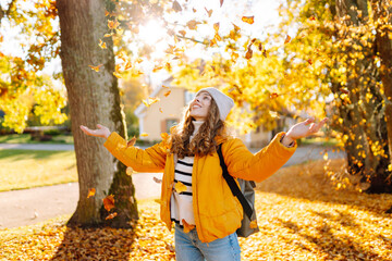 A happy woman stands in an autumn park and cheerfully throws colorful leaves up. A young woman in a...