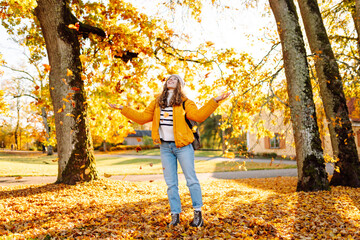 A happy woman stands in an autumn park and cheerfully throws colorful leaves up. A young woman in a...