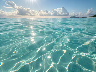 Clear turquoise ocean water shimmers under sunlight with clouds on the horizon