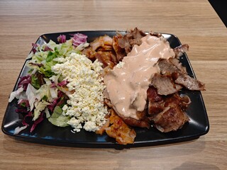 Delicious doner kebab plates with seasoned meat with fresh vegetables and cream sauce, served on a black plate