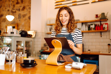 A young female barista stands behind a bar counter with prepared coffee. A beautiful woman with a...