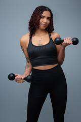 Charming brown skinned fit woman performing dumbbell biceps curls. Perfect for fitness training,...