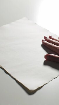 A clean, well-groomed hand gently adjusts a pristine, subtly textured natural white paper with soft deckled edges on a seamless white surface, enhanced by soft studio lighting and bokeh. Concept of