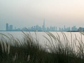 Cinematic Dubai City skyline at twilight, soft focus on green grass in foreground reflecting on...