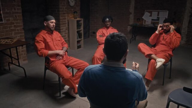 Full arc shot of middle-aged Caucasian male psychologist conducting therapy session for group of defiant multiethnic inmates convicted for gang violence crimes, attending rehabilitation program