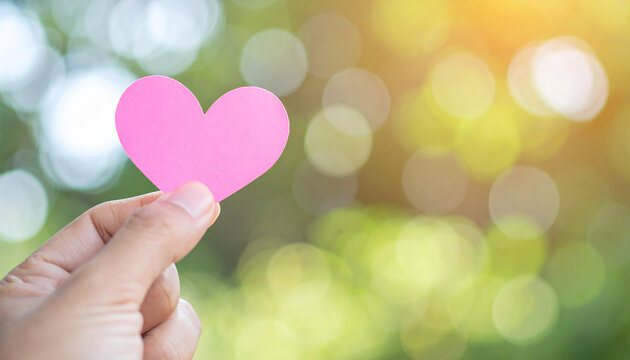 Pink heart held by hand against soft natural background. Love, care and emotional support. - Powered by Adobe