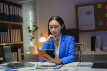 Focused businesswoman using calculator and working late at night in office