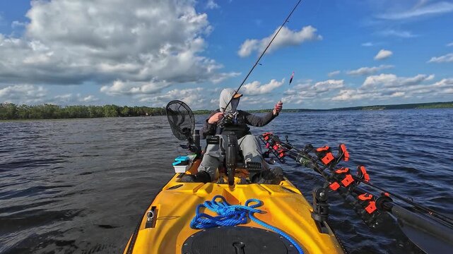 Angler in sun screen hoodie and hat catch and release small panfish while on fishing kayak. Leisure in solitude in the middle of the lake at sunny cloudy day. Bluegill fish and bobber line on camera.