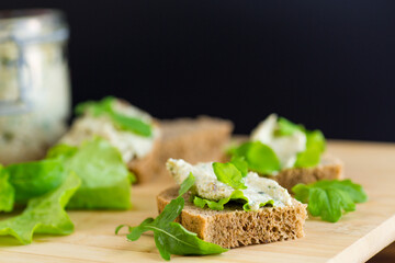 Slice of rye bread with cheese spread and greens on the table