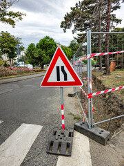 Roadwork warning sign indicating lane narrowing on the left, placed on an urban street under construction