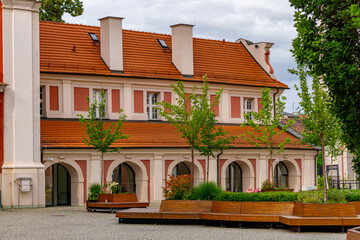 Historic Poznań City Hall building with a red roof and arcades, surrounded by benches and young...