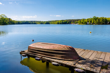 Old rusty overturned boat chained to a small wooden pier. Beautiful summer lake.