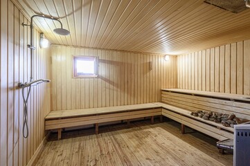 cozy sauna with wooden walls, ceiling, and benches. A shower is visible on the left. The room has a small window