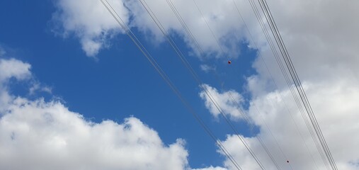 High-voltage power lines against a blue sky with white, fluffy clouds. A concept of energy, infrastructure, communication, data transfer, and global networks. Cloudy background.