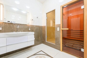 modern bathroom featuring a white vanity, tiled walls, a glass-enclosed shower, and a sauna with a...