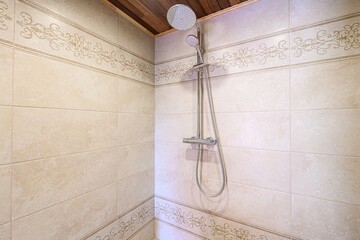 shower with beige tiles, decorative accents, and a chrome shower head. The ceiling has a natural...