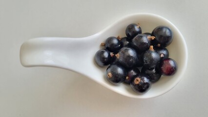 White ceramic vase with a curved handle contains several glossy blackcurrants. 