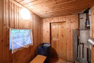 rustic sauna room with wooden walls, ceiling, and door. Contains a blue barrel, bench, and a window...