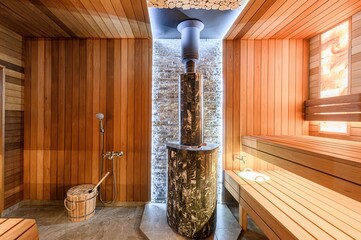 luxurious sauna interior features wooden paneling, tiered benches, a stone-clad heater, a rustic water bucket, and soft lighting for a relaxing spa-like atmosphere