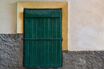 Close-up of a small green door on a grey, yellow and light pink wall, Italy