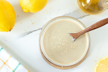 White sauce with tahini and lemon in a bowl with wooden spoon. Top view.
