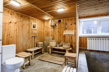 sauna room with wooden walls and ceiling, wooden benches, buckets, and a toilet