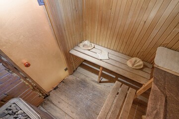 cozy sauna room with wooden benches, walls, and floor. Accessories like hats and a glove are neatly...