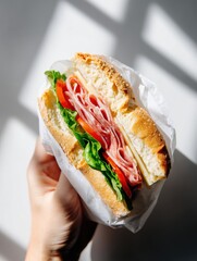 Delicious ham and cheese sandwich held in hand, wrapped in white paper, food magazine style photo for advertising and promotional use, magazine styling