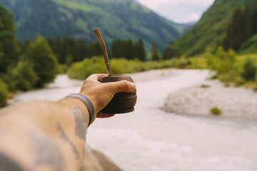Tourist holding calabash with yerba mate in mountain river landscape