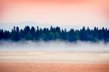 Sunrise Sunset on Lake with Mist Rising from Water Pine Trees and Mountains in Background
