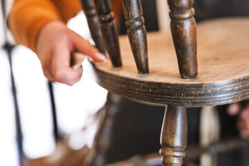 Closeup of sanding aged chair with piece of sandpaper in workshop. Small business