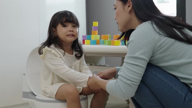 mother is helping toddler gir learning sit on toilet wc seat at home. child being potty trained