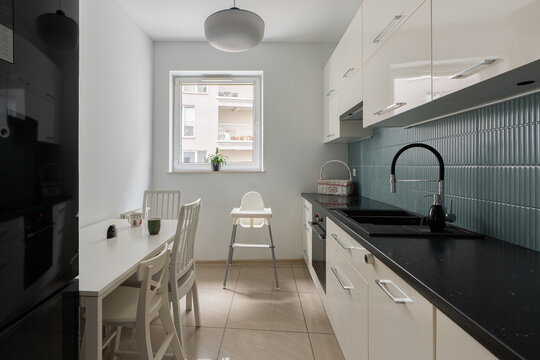 Family kitchen interior in a real estate property with a baby high chair at the dining table. Home for parents with an infant for feeding and eating meals. A modern family lifestyle.